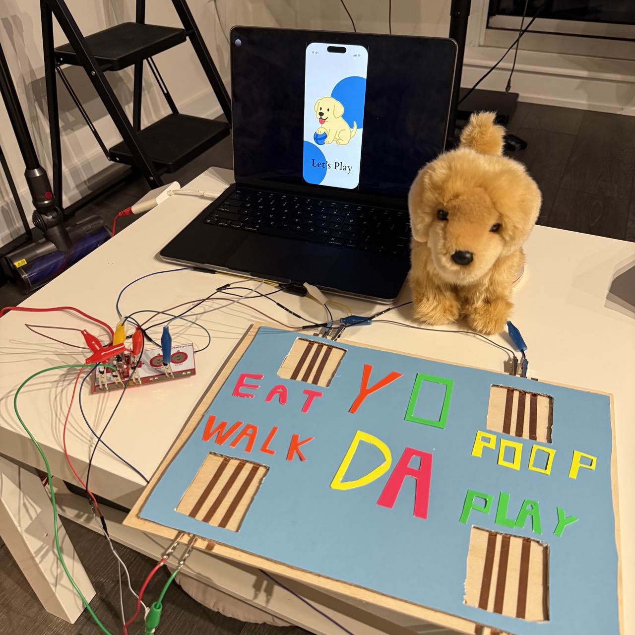 This photo shows my completed four-zone communication mat connected to Makey Makey and ProtoPie. Each labeled stepping area (“EAT,” “WALK,” “POOP,” “PLAY”) is built with pressure-sensitive copper-tape sensors under a decorated wooden board. When the plush dog steps on a zone, the system triggers the corresponding message and animation on the laptop screen. This final setup demonstrates how a pet-friendly physical interface can translate simple actions into clear digital communication.https://youtube.com/shorts/JMjwChwgOG0?si=W5AUq-MdXvdYf65a